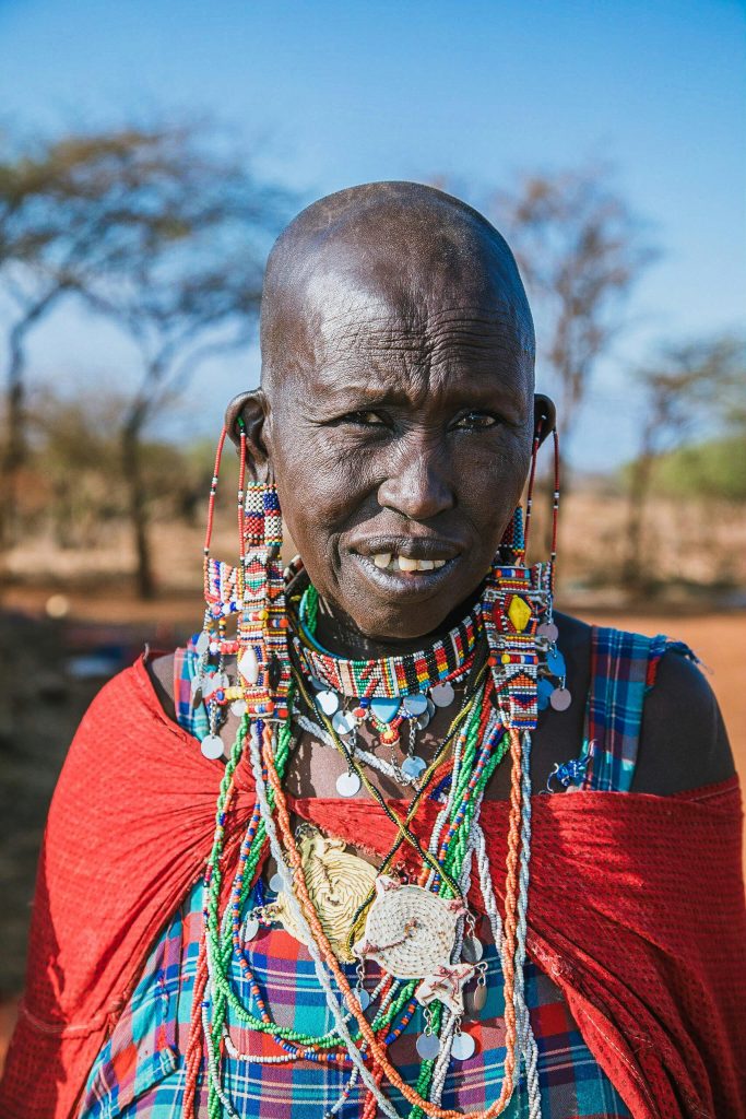 A vibrant Maasai woman in traditional attire smiles in the Kenyan landscape.