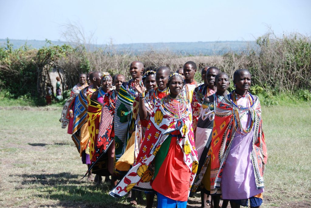 Group of Maasai women wearing traditional attire in a rural outdoor setting.