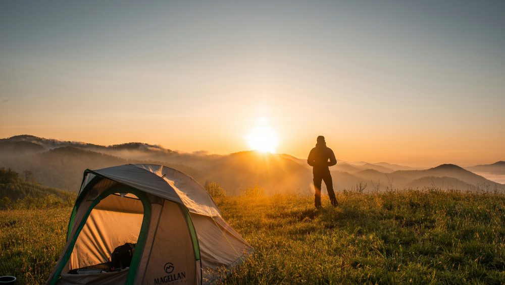 A camper enjoys the sunrise in a mountain setting with a tent. Perfect nature escape.