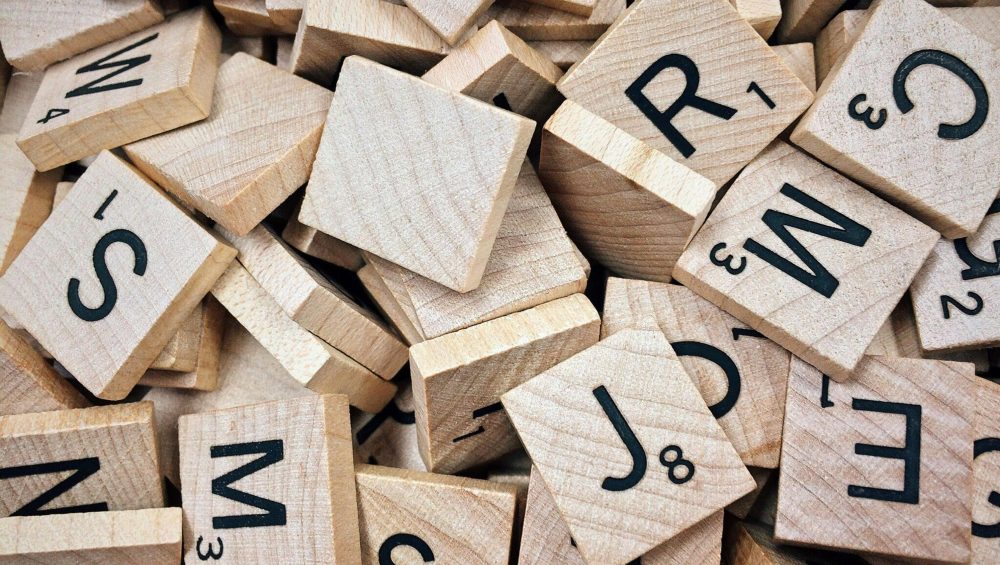 A collection of wooden Scrabble tiles with letters and numbers stacked randomly.