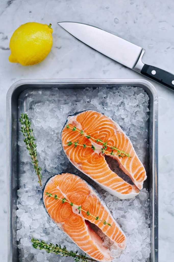 Top view of fresh salmon steaks on ice with lemon, thyme, and knife, showcasing culinary freshness.