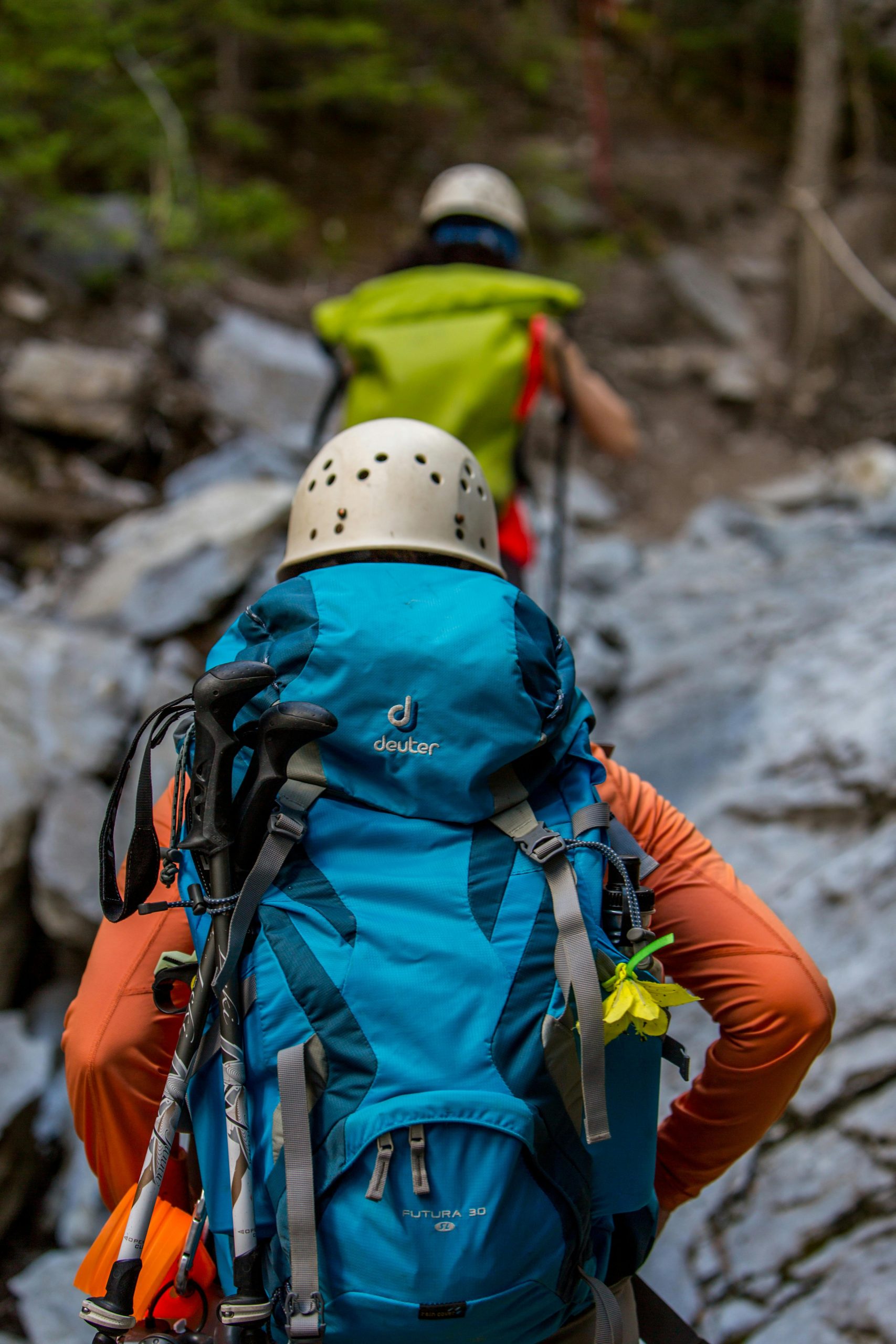 Trekking with Purpose Two hikers with backpacks and helmets navigating a rocky trail in the forest.