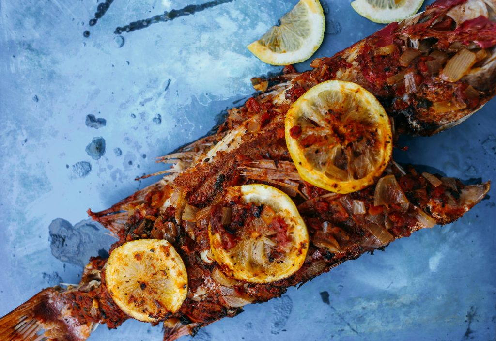 Deliciously grilled fish topped with lemon slices on a textured blue surface.