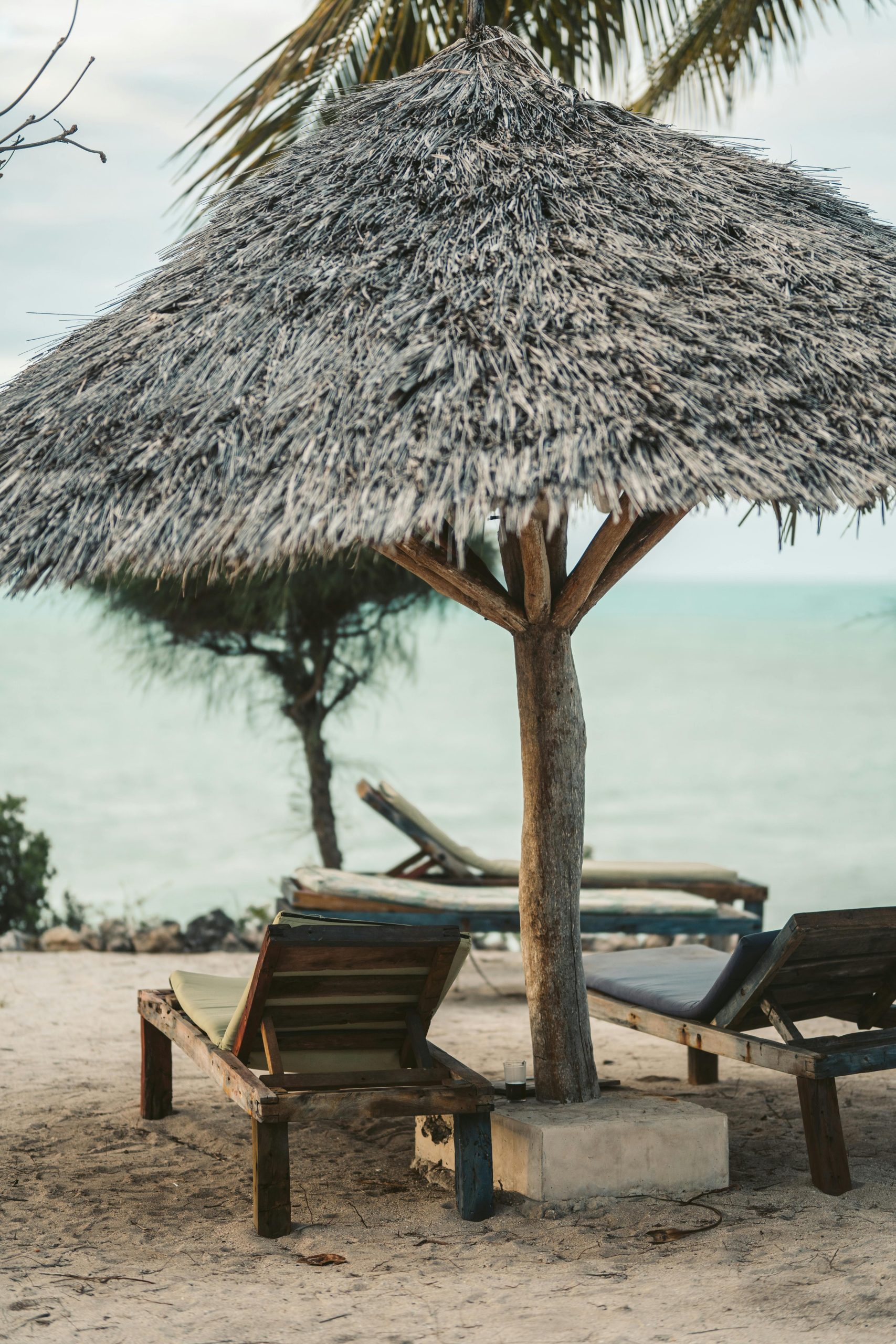 Relaxing beach scene with wooden loungers under a thatch sunshade in Zanzibar.