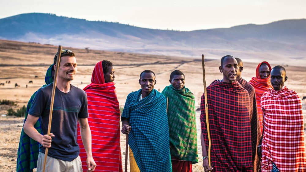 A traveler joins Masai tribe members on a sunny day in an open African landscape.