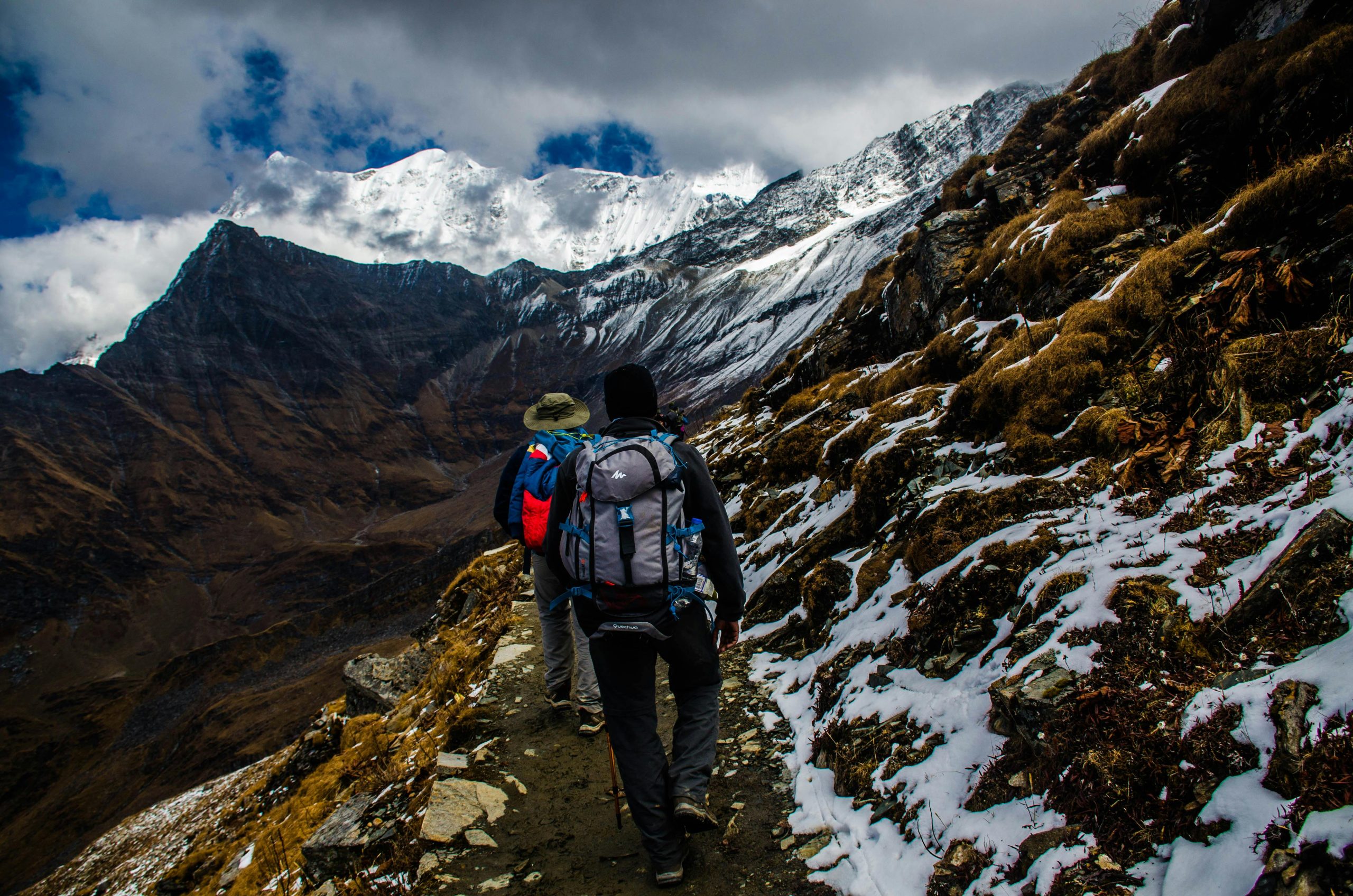 Trekking with Purpose Two hikers navigating a snowy trail in rugged mountainous terrain under dramatic skies.