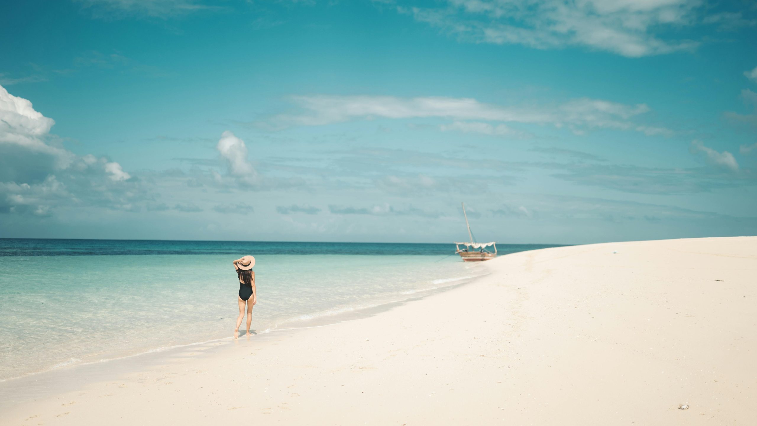 A woman enjoys a peaceful stroll on the sandy shores of Zanzibar, Tanzania.
