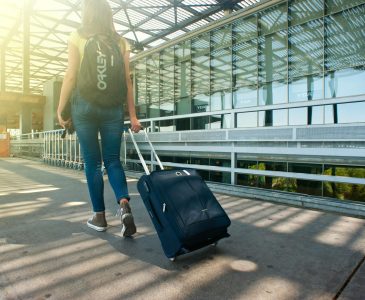 A woman walks with a suitcase outside an airport terminal, ready for travel.