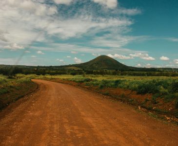 Explore the serene beauty of a rural dirt road winding through the lush Tanzanian countryside under a bright sky.