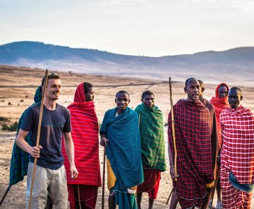 A traveler joins Masai tribe members on a sunny day in an open African landscape.